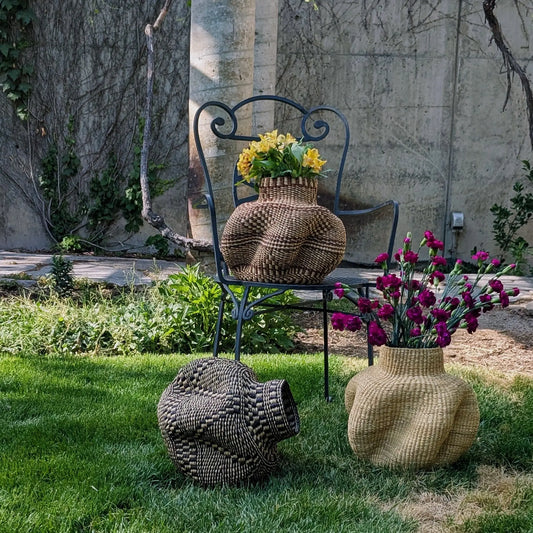 Woven vases with flowers on a chair and ground in a garden setting