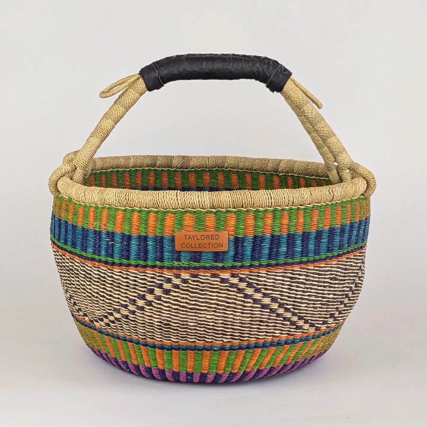 Woven basket with colorful patterns and a black handle on a light gray background