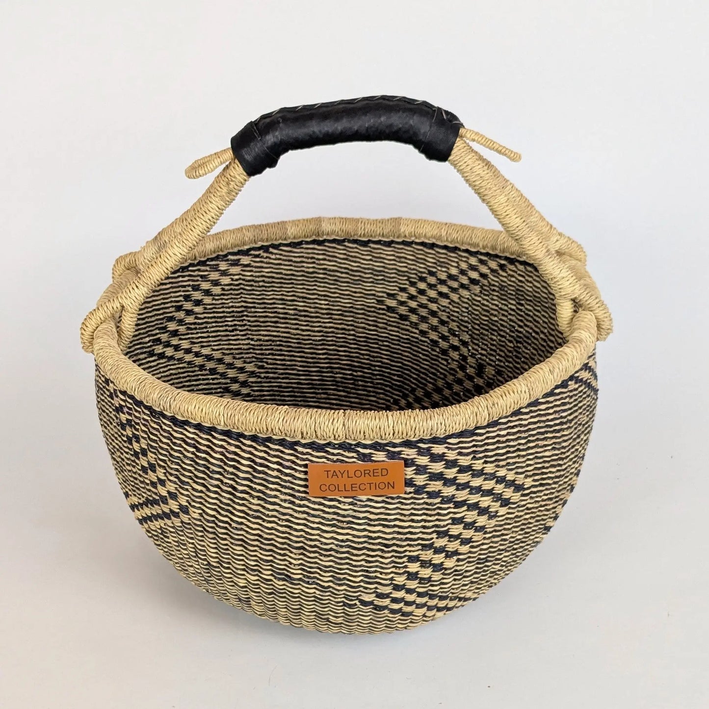 Woven basket with black handle and visible brand label on a white background