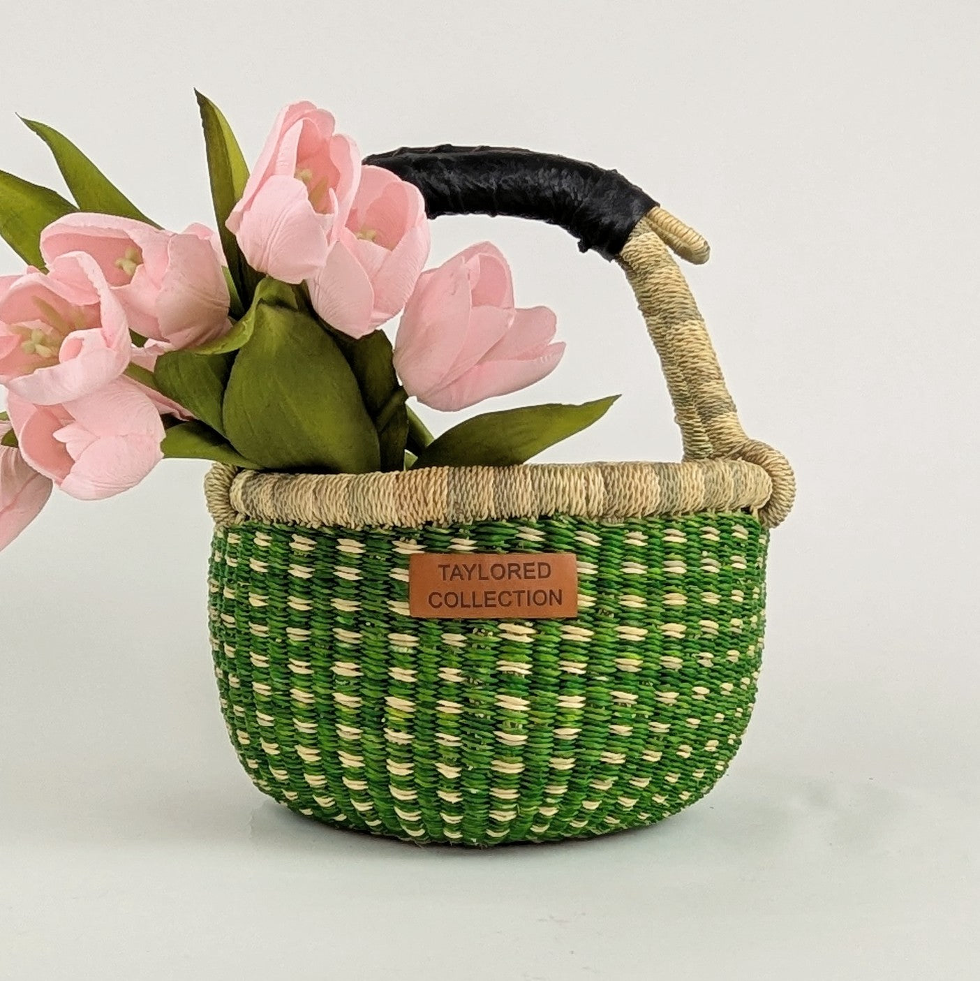 Handwoven Bolga basket in green with a black leather-wrapped handle holding soft pink tulips