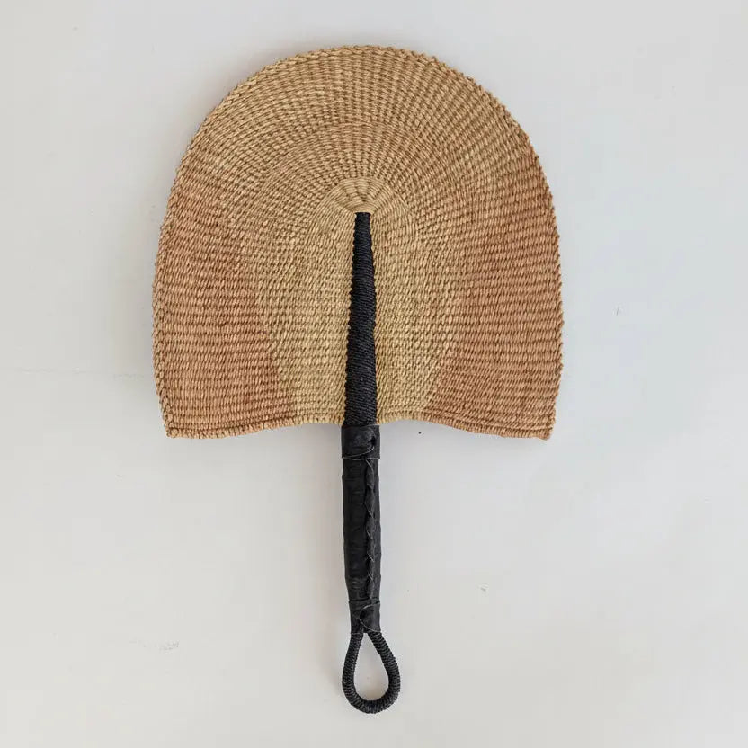 Woven fan with a black handle on a light beige background