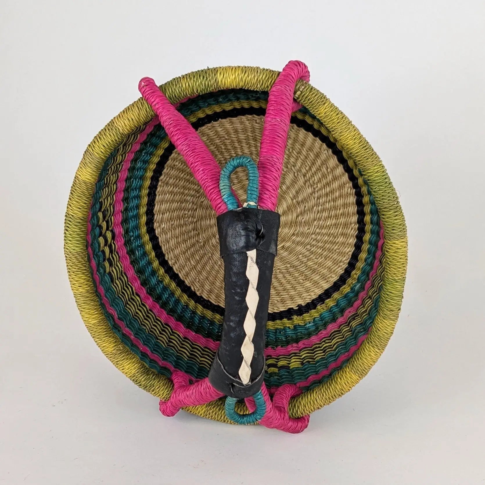 closeup of a colorful woven basket with a black leather wrapped handle on a white background