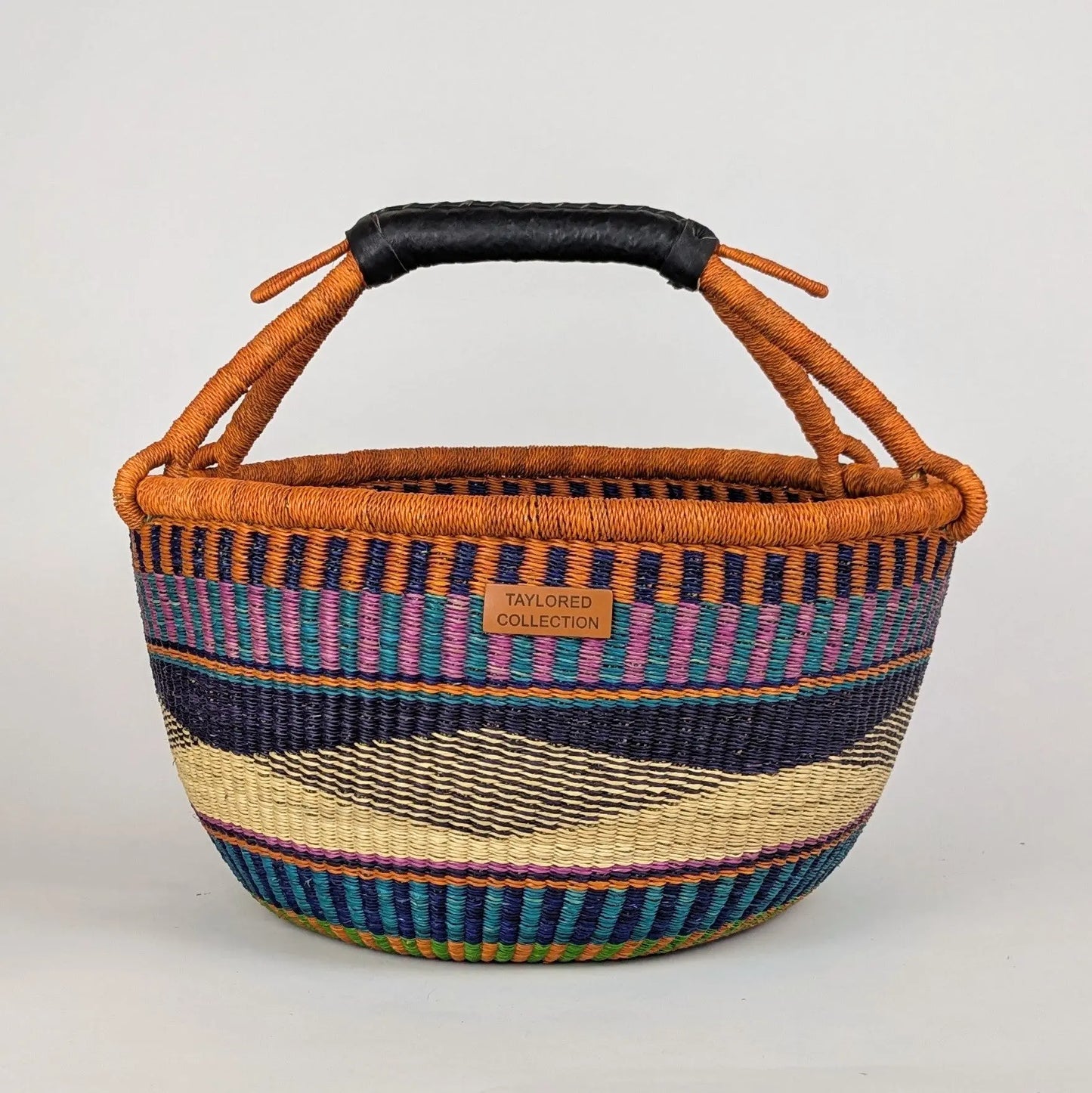 Woven basket with striped pattern and orange handle on a light gray background