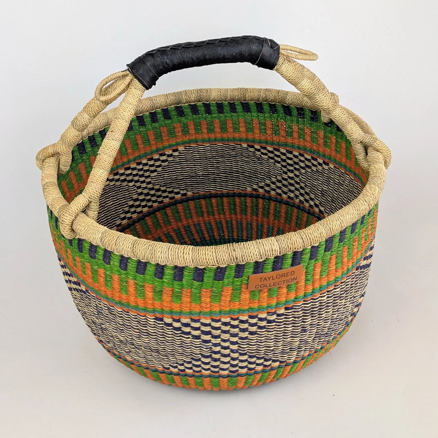 Woven basket with colorful pattern and black handle on a white background
