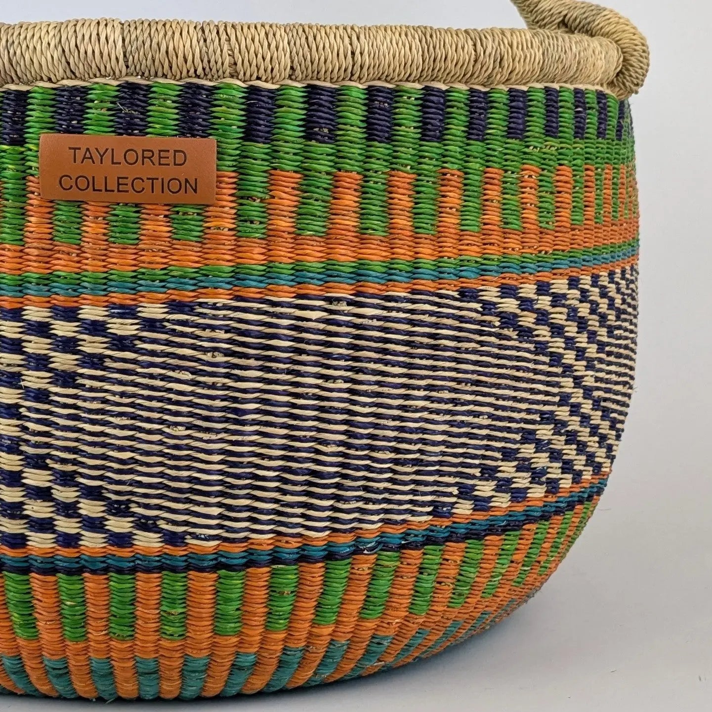 Woven basket with colorful pattern and 'Taylored Collection' label on a gray background