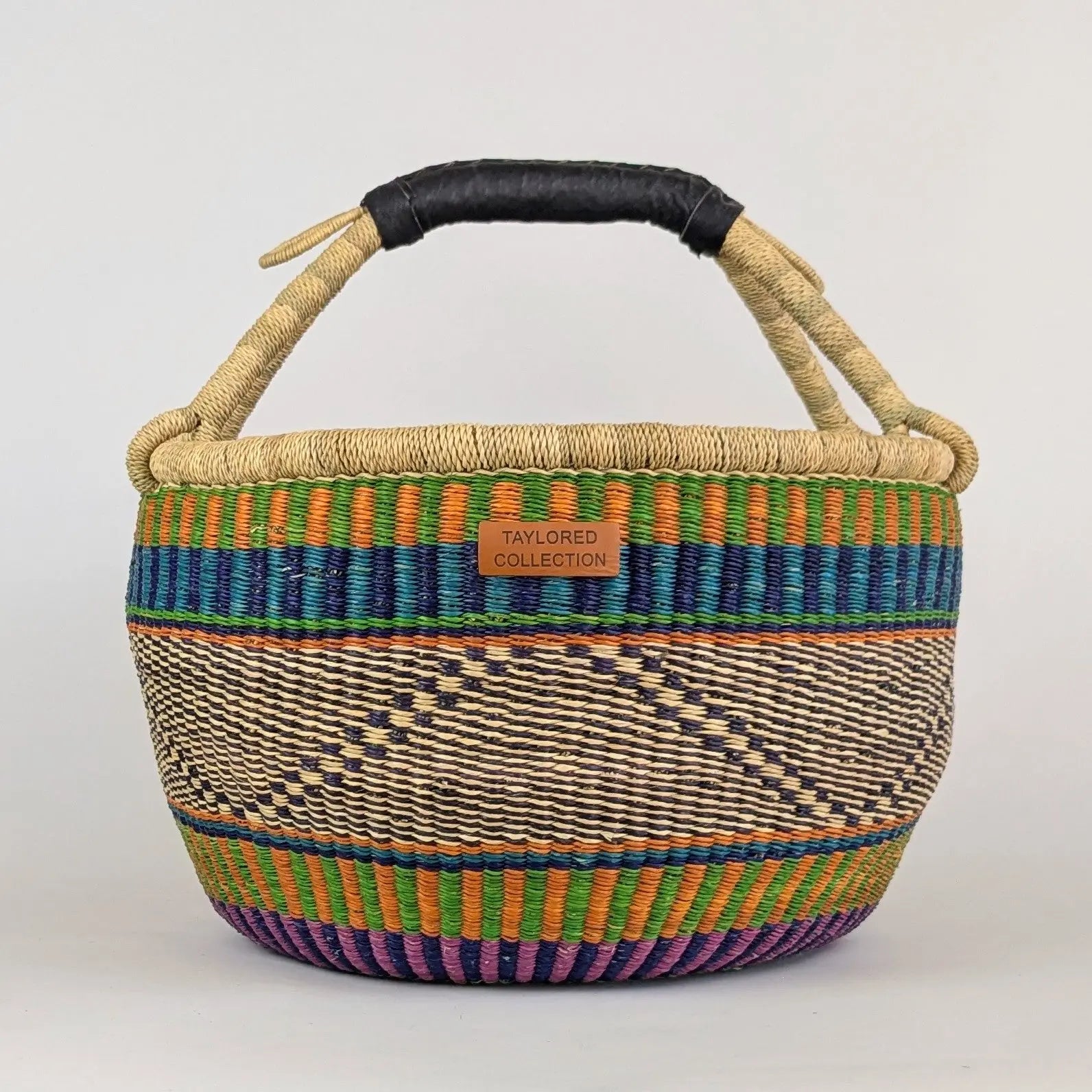 Woven basket with colorful patterns and a black handle on a light gray background