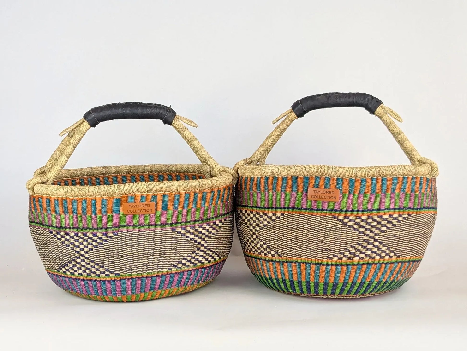 Two woven baskets with colorful patterns and black handles on a white background