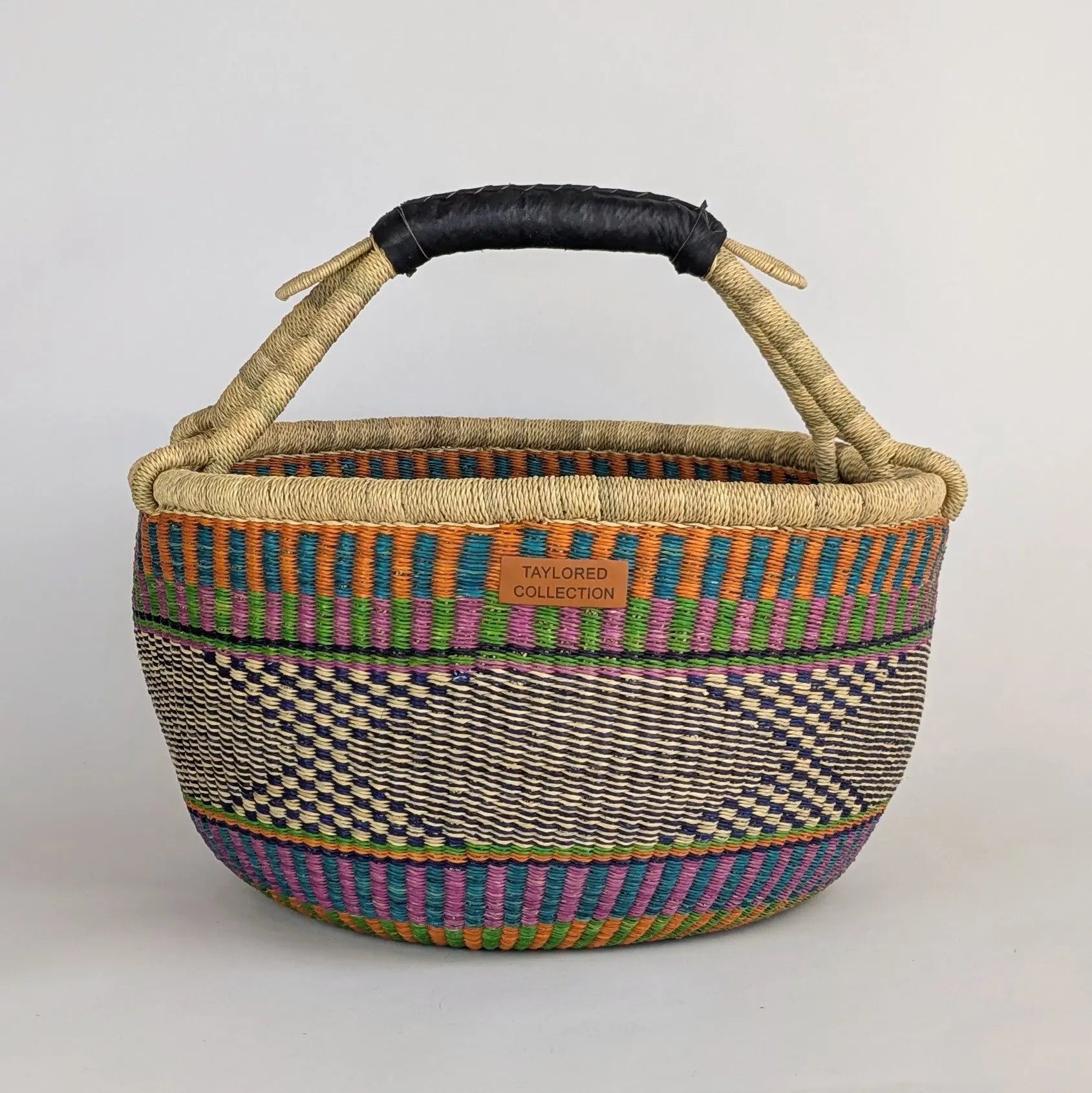 Woven basket with colorful pattern and black handle on a light gray background