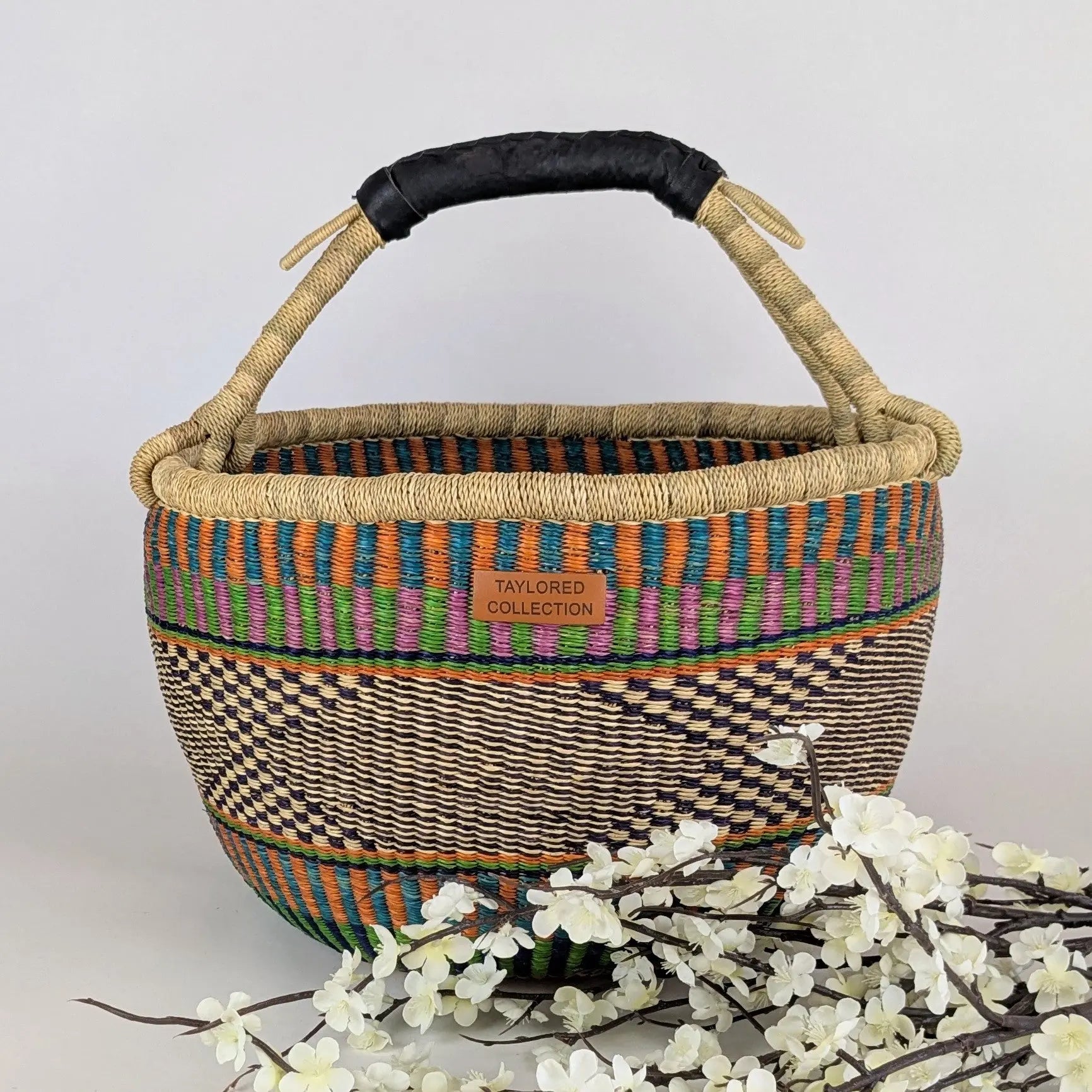 Woven basket with colorful patterns and a black handle on a light gray background