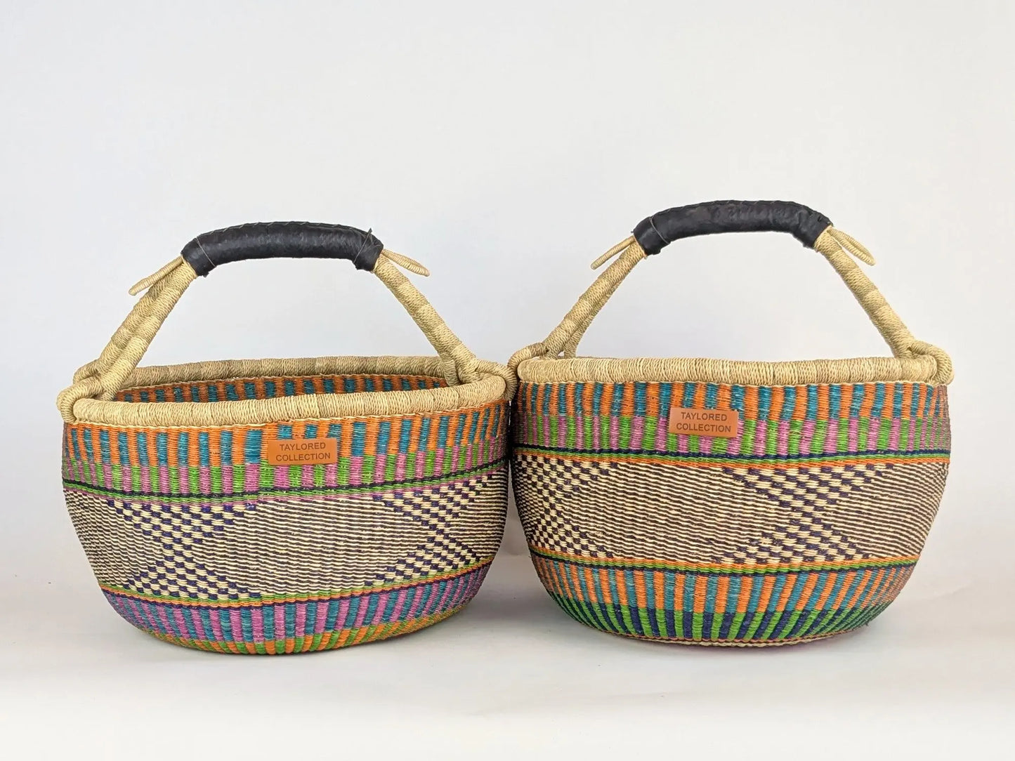 Two woven baskets with colorful patterns and black handles on a white background