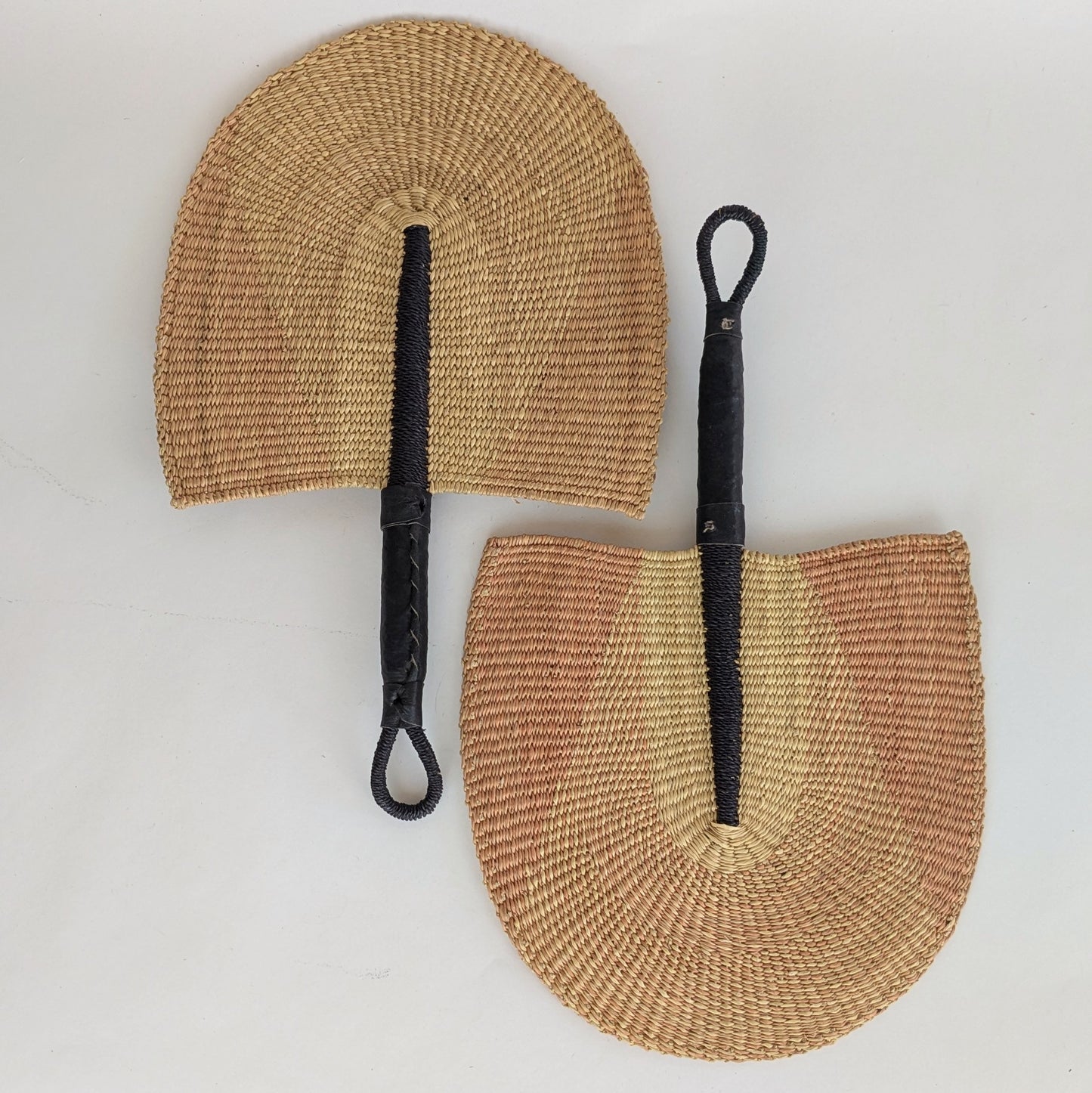 Two woven fans with black handles on a white background